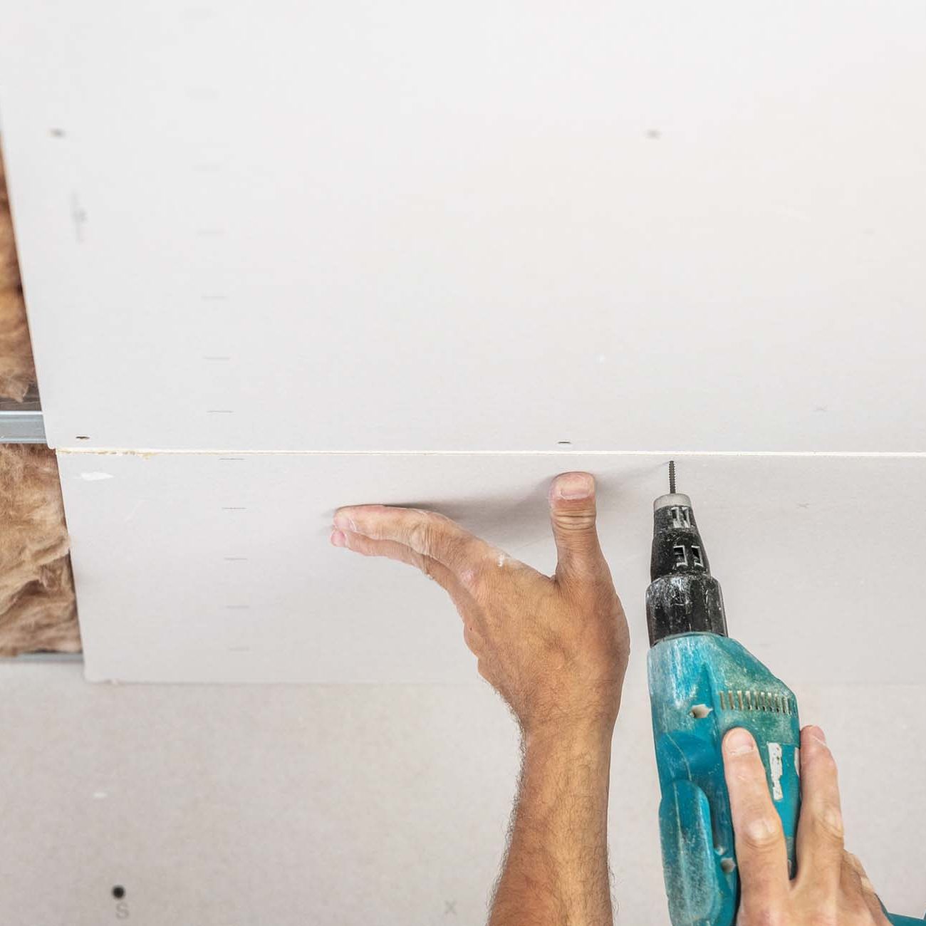 Hand putting up plaster board with a drill